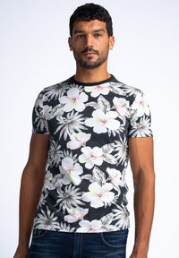 Černé tričko s krátkým rukávem, které má květinový vzor s velkými bílými a růžovými květy hibiscus a zelenými akcenty, vyrobené z měkkého materiálu.