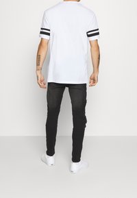 White short-sleeve t-shirt with black stripes on the sleeves, paired with distressed black jeans and white sneakers.