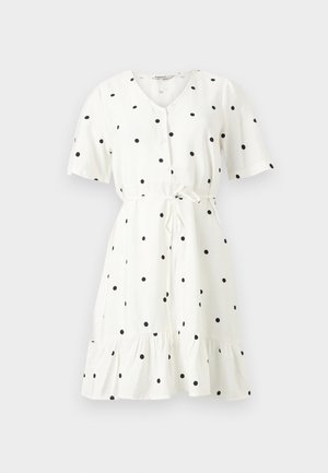 Λευκό φόρεμα με κοντά μανίκια και μήκος έως το γόνατο, με μαύρες πουά βούλες, κουμπιά στο μπροστινό μέρος, ζώνη στη μέση και βολάν στο τελείωμα, πάνω σε απλό φόντο.