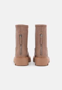 Botas de cuero marrón hasta el tobillo con cremalleras laterales, un acabado texturizado y suelas de goma gruesas. Presentan costuras verticales y una punta redondeada.