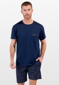Mörkblå bomullströja med ett mönstrat bröstfickat; matchad med blomtryckta shorts i mörkblåa, röda och blå variationer.