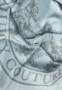 Světlomodrá tkanina se hedvábnou texturou, která obsahuje šedou zvířecí motivaci a výtvarné designové prvky, včetně kulatého emblému.