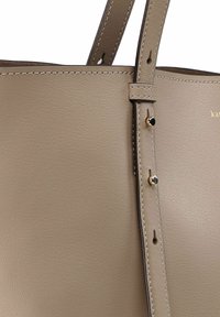 Handtas van beige leer met een gladde textuur, bovenhandvatten en stikdetails. Voorzien van een gouden logo en metalen klinknagels als detail.