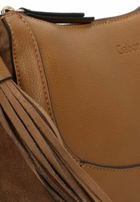 Bolso de mano de cuero marrón con textura suave, costuras en contraste y acentos con flecos a un lado, con cierre con cremallera.