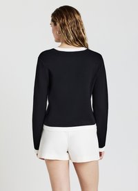 Schwarzer Pullover mit langen Ärmeln, weißem Kragenrand und geripptem Muster, kombiniert mit weißen Shorts, von hinten gezeigt.
