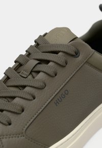 Olivenfargede skinn-sneakers med teksturert finish, runde lisser og subtil merking. Har en kontrasterende off-white såle.