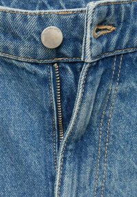 Dettaglio ravvicinato di una cerniera di jeans blu parzialmente aperta sotto il bottone metallico della vita, con dettagli di cucitura visibili.