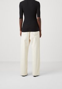 Černý žebrovaný top s krátkým rukávem kombinovaný s volnými béžovými kalhotami s širokými nohavicemi, které mají vysoký pas a žádné viditelné vzory.