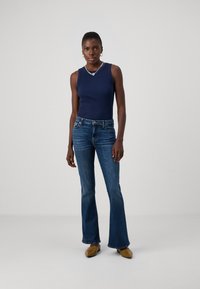 Marine-ribbet tanktopp parret med blå flared jeans. Karamellfargede slip-on sko. Enkle sølv smykkeakenter. Nøytral bakgrunn.