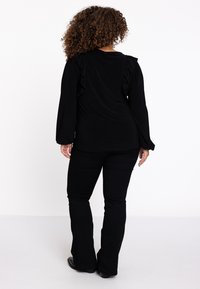 Schwarzes Oberteil mit Rüschendetails an den Schultern, langen Ärmeln, kombiniert mit schwarzen engen Hosen. Glatte Textur, figurbetontes Design und ohne sichtbare Muster.