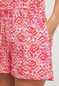 Shorts à motifs roses et blancs avec un design en losanges et des accents orange, une taille à cordon et des poches latérales.