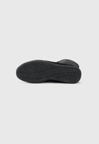 Černá podrážka tenisky s texturovanými vzory běhounu. Vyrobena z gumy s hladkým povrchem a tvarovaným tvarem pro lepší trakci a stabilitu.