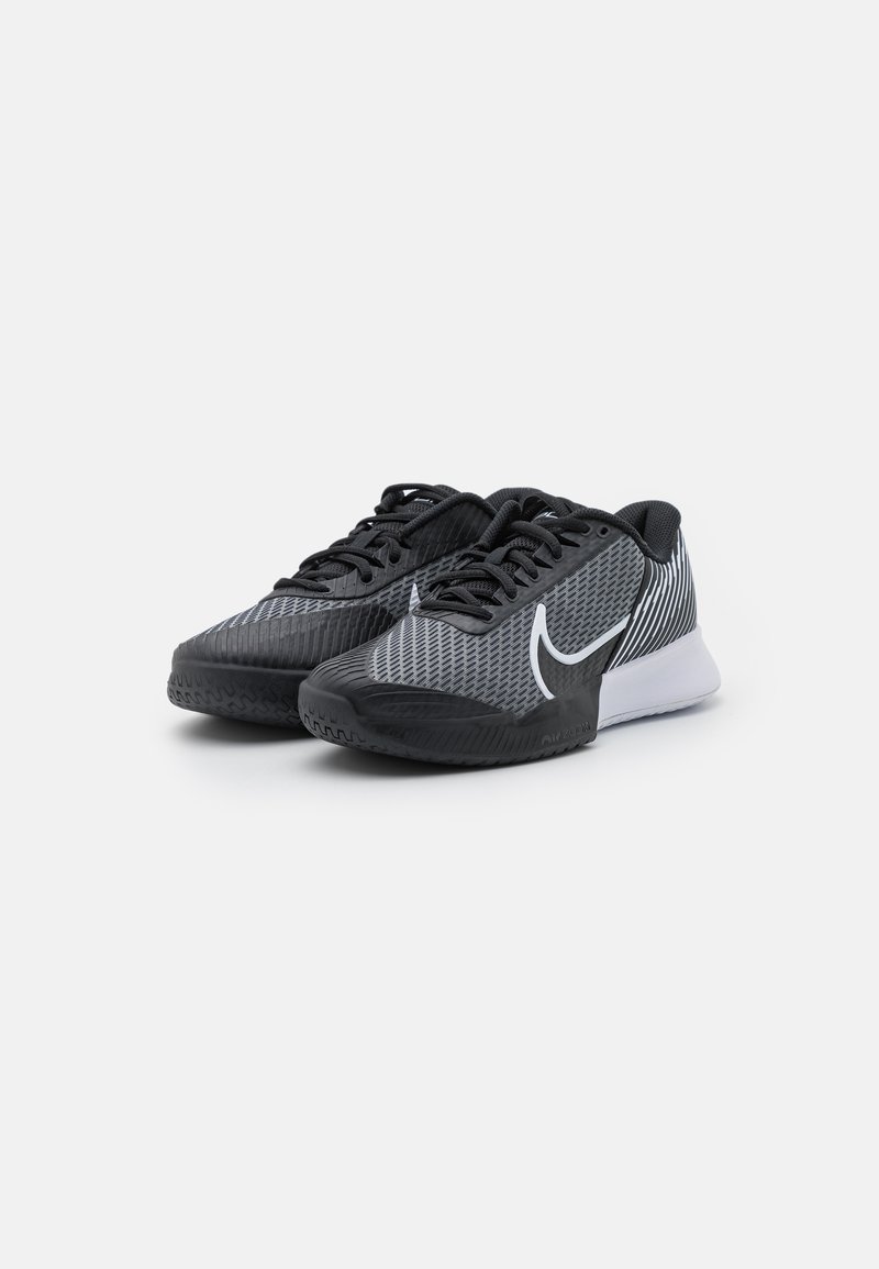 Une paire de chaussures de sport noires et grises avec un logo swoosh blanc, un design en maille et des semelles épaisses, légèrement inclinées vers la droite sur un fond blanc.