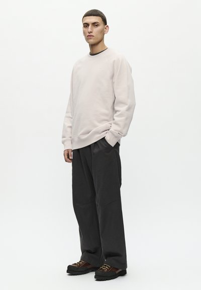 Helles rosa Sweatshirt mit gerippten Bündchen und Saum, kombiniert mit dunklen, lockeren Hosen. Schwarze und braune Sneaker runden das Outfit ab.