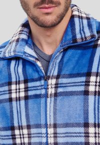 Chaqueta de forro polar azul con un patrón de cuadros en azul oscuro, blanco y negro, con cierre de cremallera y un acabado suave y texturizado.