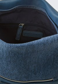 Borsa a tracolla blu in pelle con una parte superiore in texture denim e fodera scura. Presenta una tasca con zip e un'etichetta del marchio all'interno.