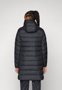 Black puffer coat with a hood, featuring a quilted design, long length, and a smooth, shiny texture. Includes side pockets and a tag.