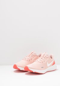 Scarpe da corsa Nike in rete rosa chiaro con accenti bianchi. Caratterizzano una superficie testurizzata, punta arrotondata e suola color corallo.