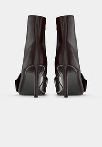 Blizgūs tamsiai burgundiški kulkšninių bateliai su elegantiška siluetu, aukštais stiletto kulnais ir užtrauktuku gale. Papuošti persidengiančiomis dalimis.