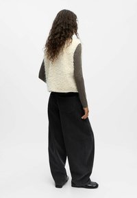 Fluffy crèmekleurige vest met grijze lange mouwen, gedragen met hoge zwarte wijde jeans en zwarte schoenen. De textuur lijkt zacht en warm te zijn.