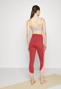 Soutien-gorge de sport violet avec des bretelles fines, associé à un legging rouge taille haute avec un design en bloc de couleurs rose sur le bas des jambes.