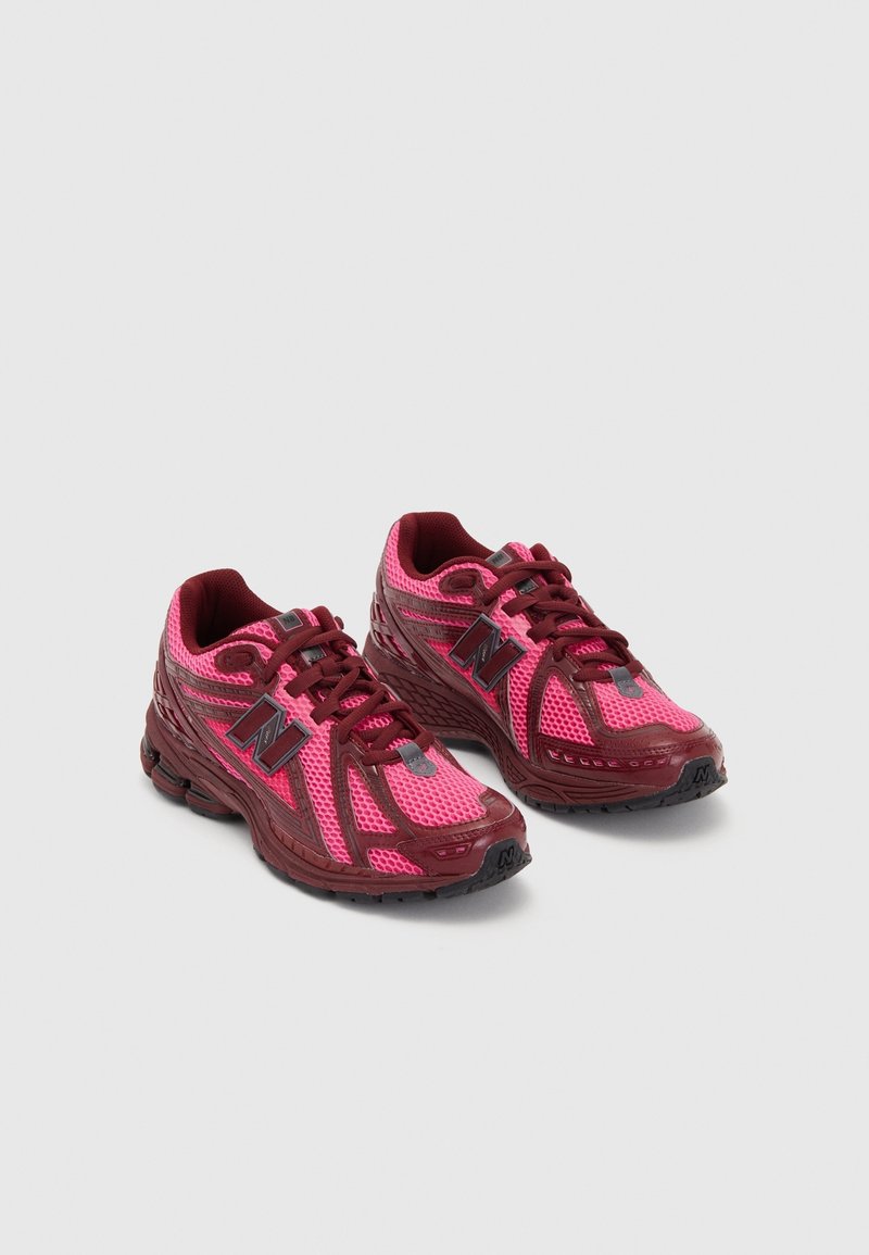 Paire de chaussures de sport New Balance roses et bordeaux avec empeignes en mesh et synthétique, lacets attachés, inclinées sur un fond gris clair.