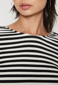 Svart og hvitstripet topp med rund hals, laget av mykt stoff, med jevnt fordelte horisontale striper og en glatt tekstur.