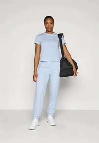 Camiseta de algodón azul claro con mangas cortas y texto blanco, combinada con joggers a juego y zapatillas blancas; sosteniendo una bolsa de deporte negra.