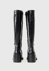 Μαύρες μπότες μέχρι το γόνατο από λαμπερό δέρμα. Διαθέτουν στρογγυλή μύτη, γερό τακούνι και φερμουάρ στην εξωτερική πλευρά για κλείσιμο.