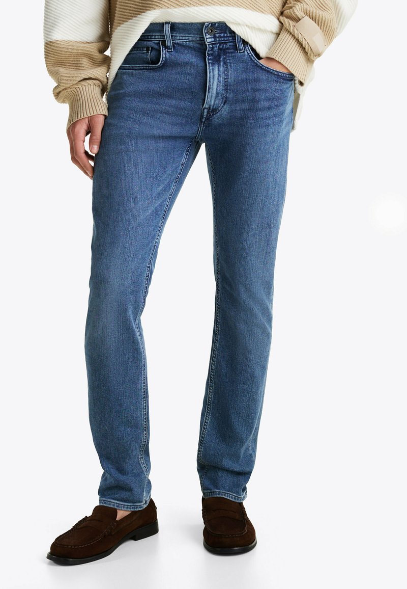 Jeans de mezclilla azul claro con un corte recto, que presentan bolsillos frontales y un acabado desgastado, combinados con mocasines de ante marrón.