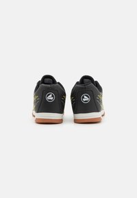 Baskets de sport noires avec une surface texturée, accents jaunes, semelle blanche et talon arrondi. Présentent un logo à l'arrière de chaque chaussure.