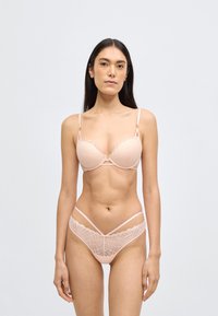 Blonde bh med blonder, bølget kant og bøjle. Matchende g-streng med geometrisk blonde mønster og krydsede stropper. Glat tekstur.
