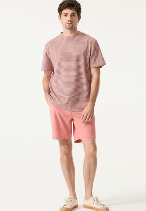 Rood-wit gestreept T-shirt met korte mouwen, gecombineerd met roze korte broek. Casual ontwerp met ronde hals. Creme kleurige schoenen maken de outfit compleet.