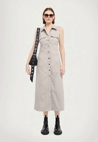 Hõbedane, põlveni ulatuv särgimekk koos esipaneeli nööpidega, kahte rinna taskut ja kraega kaelus. Ühildatud mustade sõjaväekingade ja kotiga.