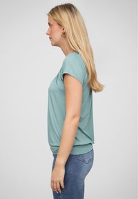 Korte mouw teal t-shirt met een relaxte pasvorm, zacht katoenen materiaal en subtiele naaddetails. Gecombineerd met blauwe denim jeans.