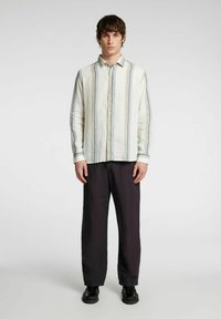 Camicia button-up in tessuto leggero con righe verticali grigie, gialle e blu. Dotata di colletto e maniche lunghe. Abbinata a pantaloni scuri.