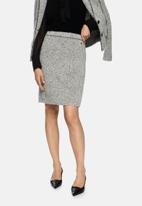 Gray textured pencil skirt with a fitted design and a fringed hem, paired with a black top and black pointed-toe heels.