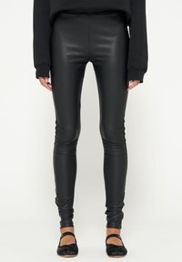 Leggings neri a vita alta in similpelle lucida, con un design aderente, fondo caviglia e lati senza cuciture.