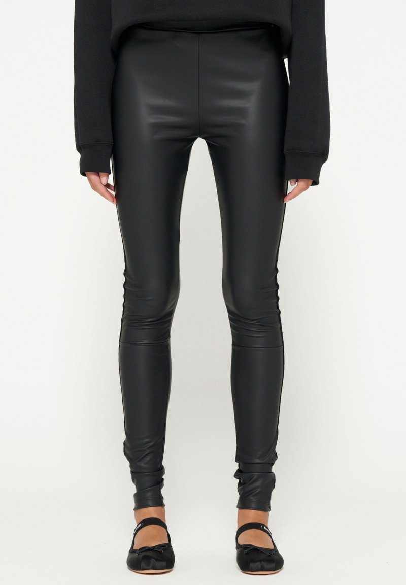 Leggings neri a vita alta in similpelle lucida, con un design aderente, fondo caviglia e lati senza cuciture.