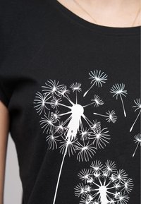 Svart T-skjorte med hvite dandeliongrafikker i ulike størrelser. Stoffet er glatt med rund hals og korte ermer.