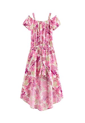 Ung kvinde iført en pink og beige floral off-shoulder kjole med høj-lav kant, stående barfodet mod en ensfarvet hvid baggrund.