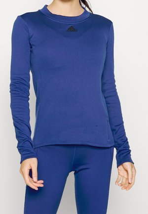 Pitkähihaista urheiluaitoa, tekstuurinen tummansininen kangas, pyöreä pääntie, Adidas-logot edessä, istuva muotoilu. Yhdistetty yhteensopivien alaosien kanssa.