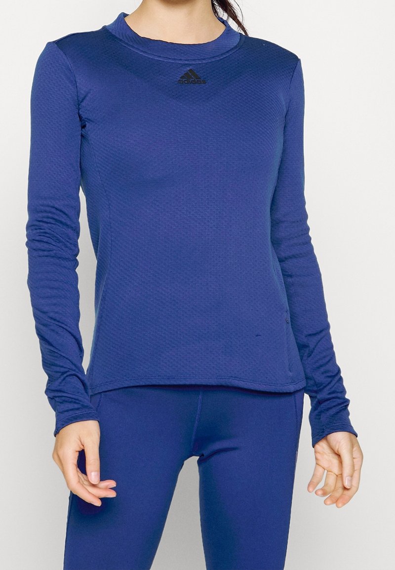 Pitkähihaista urheiluaitoa, tekstuurinen tummansininen kangas, pyöreä pääntie, Adidas-logot edessä, istuva muotoilu. Yhdistetty yhteensopivien alaosien kanssa.
