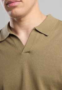 Khaki polo pusero lyhyillä hihoilla, jossa on V-pääntie ja sileä, tekstuurinen kangas perinteisellä kauluksella.