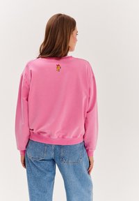 Różowa bluza z miękkiego materiału, z okrągłym dekoltem i ściągaczami przy mankietach. Posiada mały wzór z kreskówką na górnej części pleców.