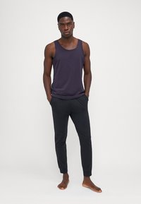 Un débardeur violet foncé associé à un pantalon de jogging noir étroit, avec des poignets élastiques et une coupe décontractée. Le matériau semble léger et lisse.
