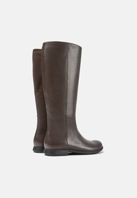 Botas de cuero marrón hasta la rodilla con un acabado suave, que cuentan con un panel texturizado en el lateral y una suela plana. Aptas para un uso versátil.