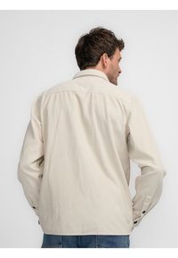 Helle beigefarbene Cordhemd mit klassischem Kragen, langen Ärmeln und Knopfmanschetten. Vertikale gerippte Textur und lockerer Schnitt.