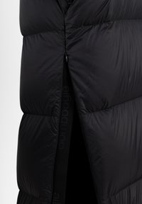 Veste rembourrée noire avec fermeture éclair, présentant des coutures en boudin, un col haut et un accent élastique avec logo le long de l'ouverture.