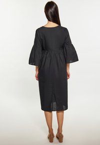 Rochie neagră cu talie strânsă, mâneci evazate și tiv până la genunchi. Fabricată dintr-un material ușor, cu o textură netedă.